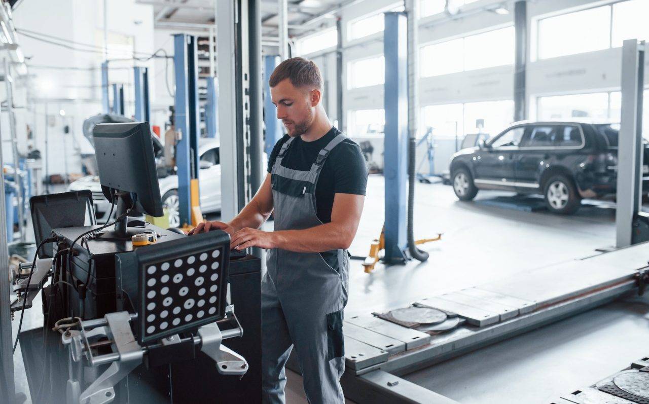 looks at keyboard man at the workshop in uniform use computer for his job for fixing broken car